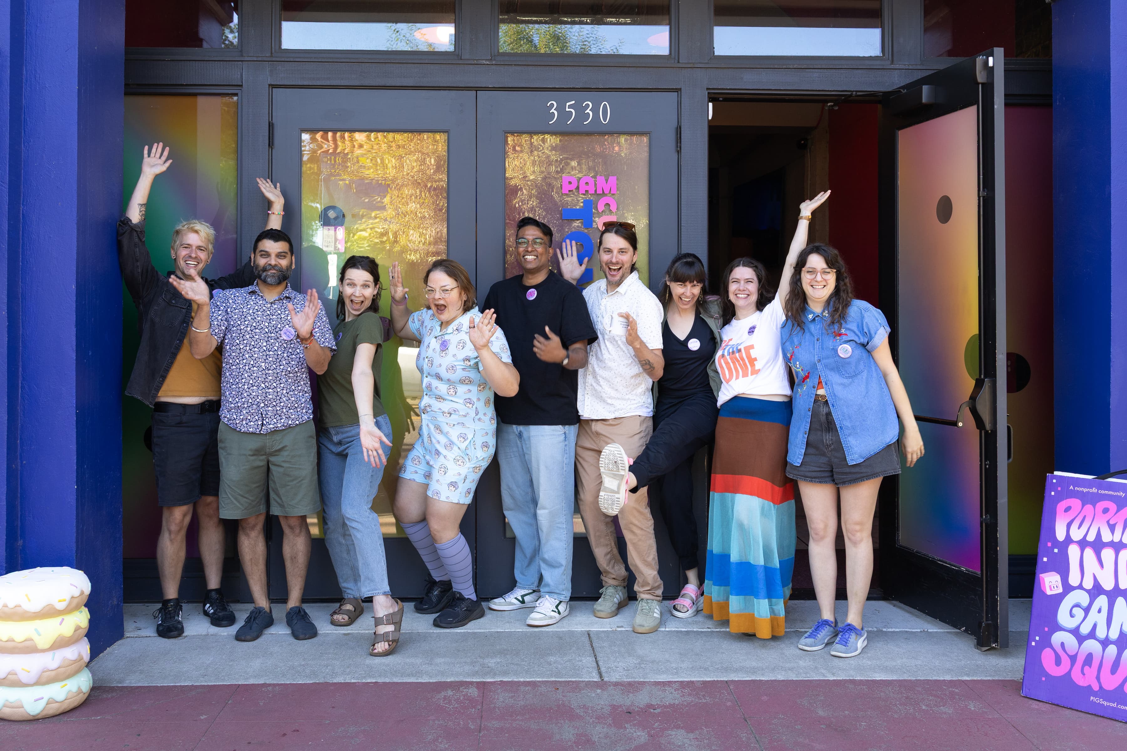 Group photo of nine of the CreativeMornings Portland volunteer standing in front of the colorful Tomorrow Theater doors smiling and throwing hands into the air