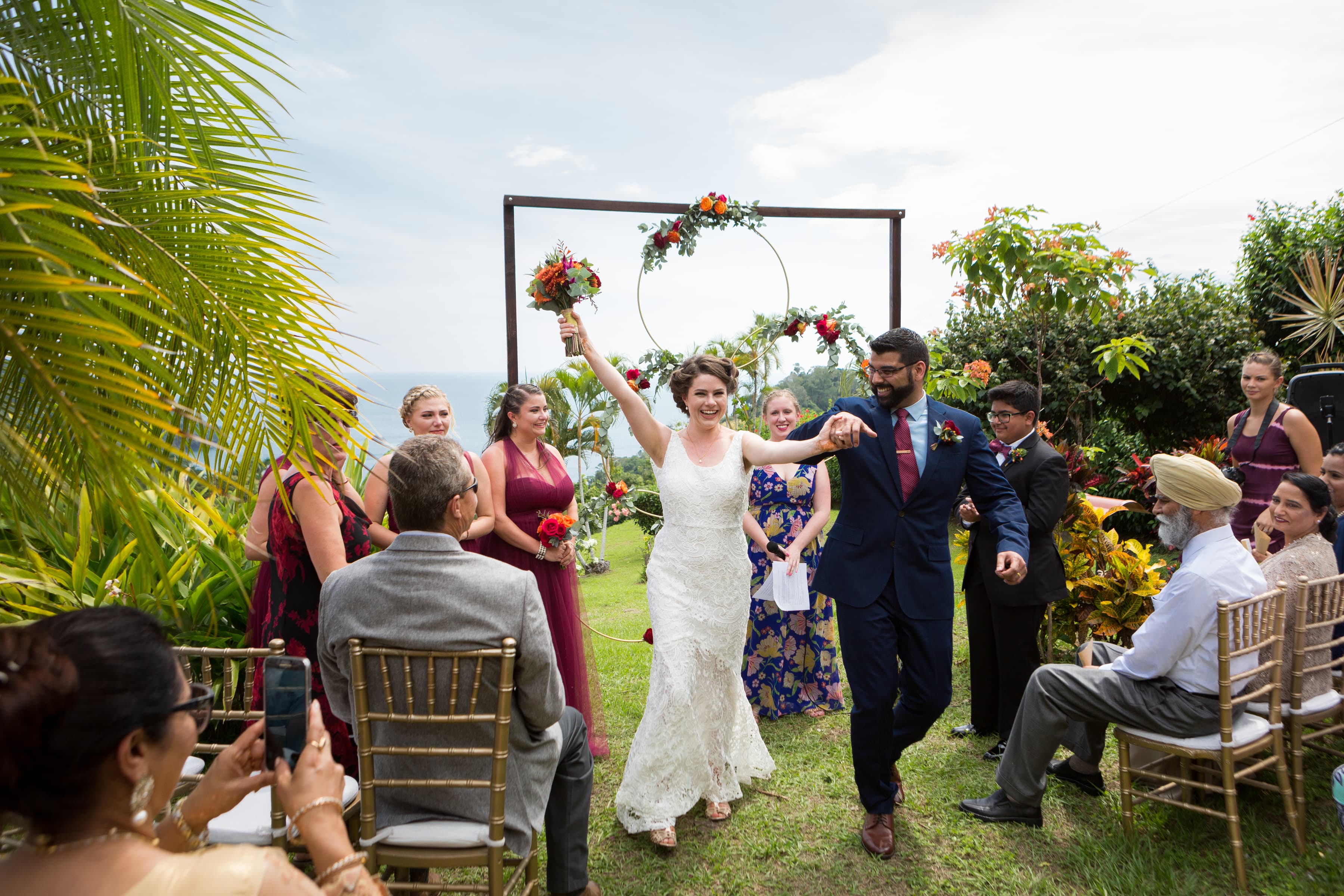 Kaitlin and her husband Sumeet holding hands and walking down the aisle at their outdoor wedding in Costa Rica